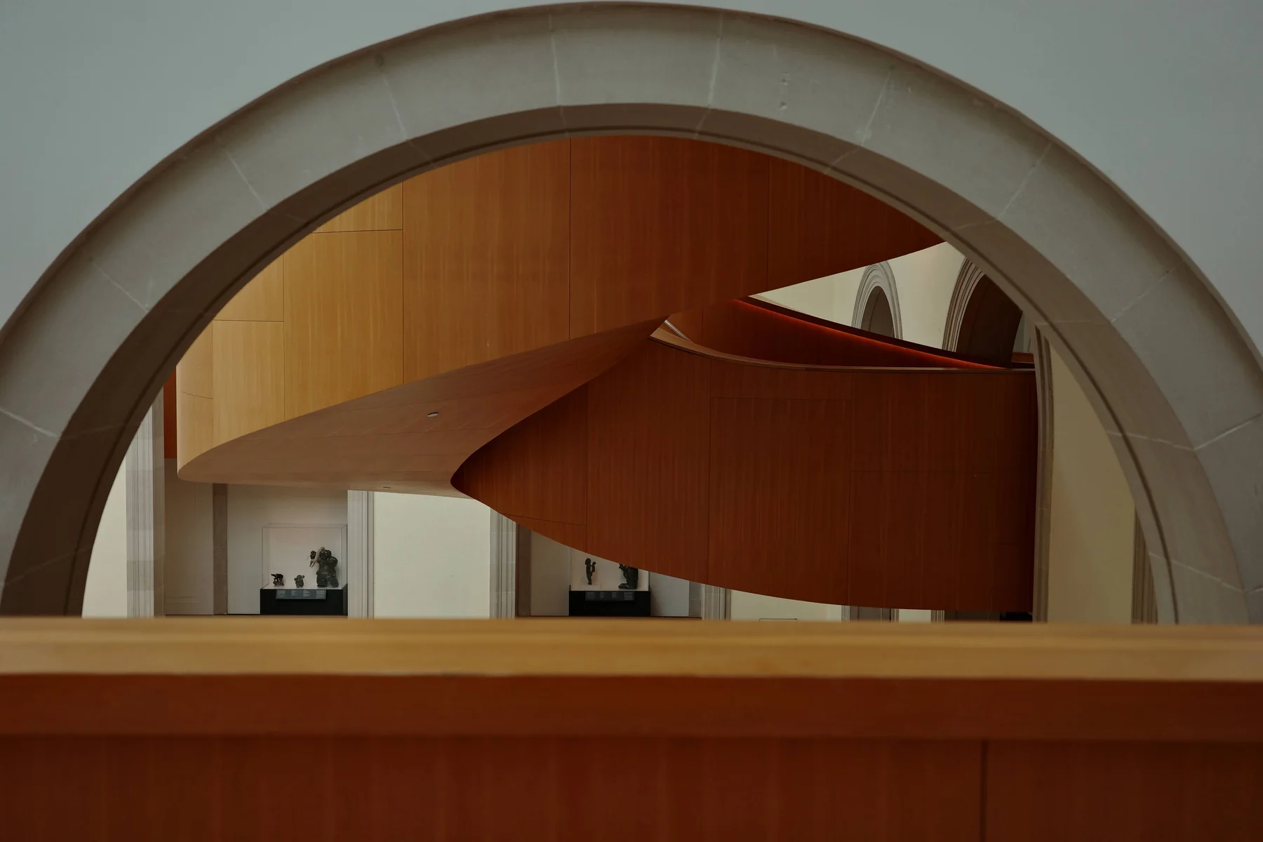 A sweeping wooden staircase framed by a pale stone arch.